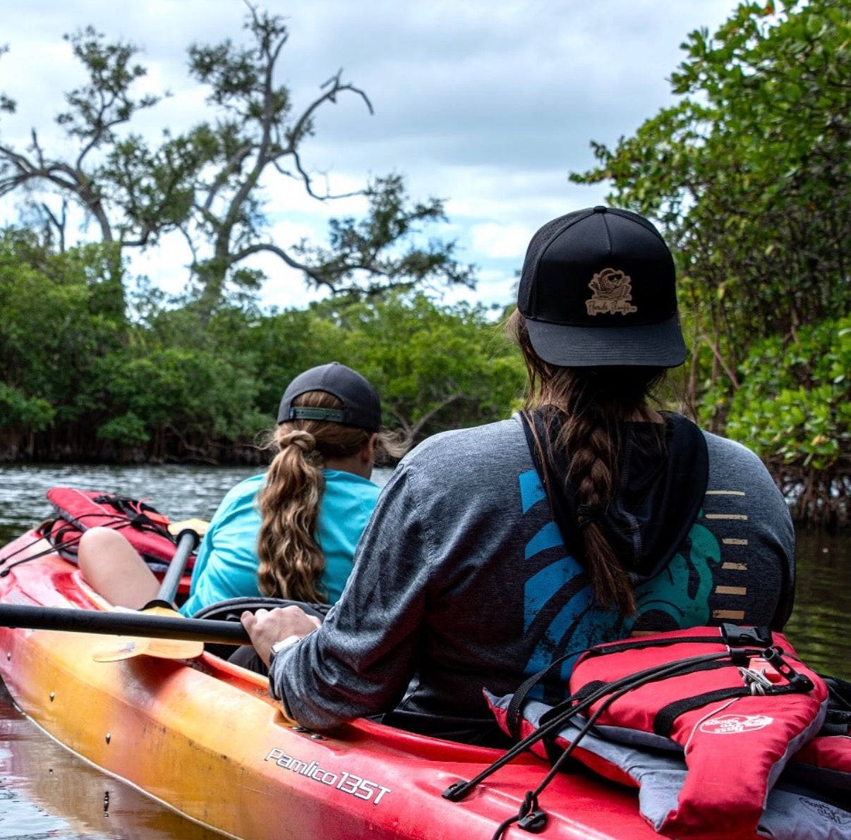 Two people kayaking in a natural setting with trees and water.