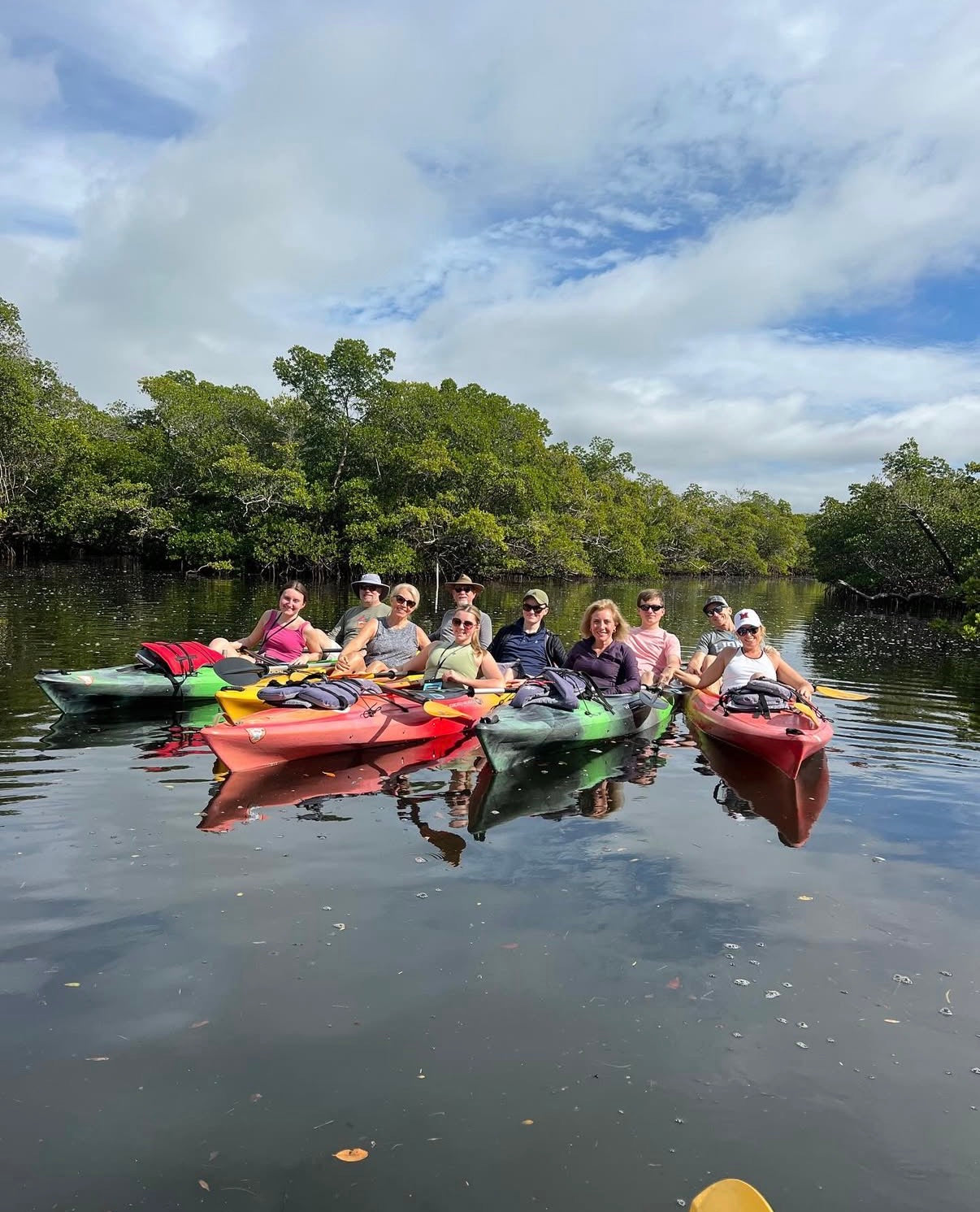 Group of people kayaking on a calm body of water with trees in the background
