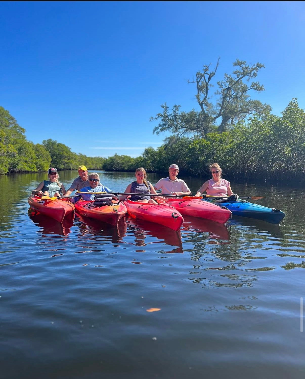 Group of people kayaking on a calm body of water with trees in the background