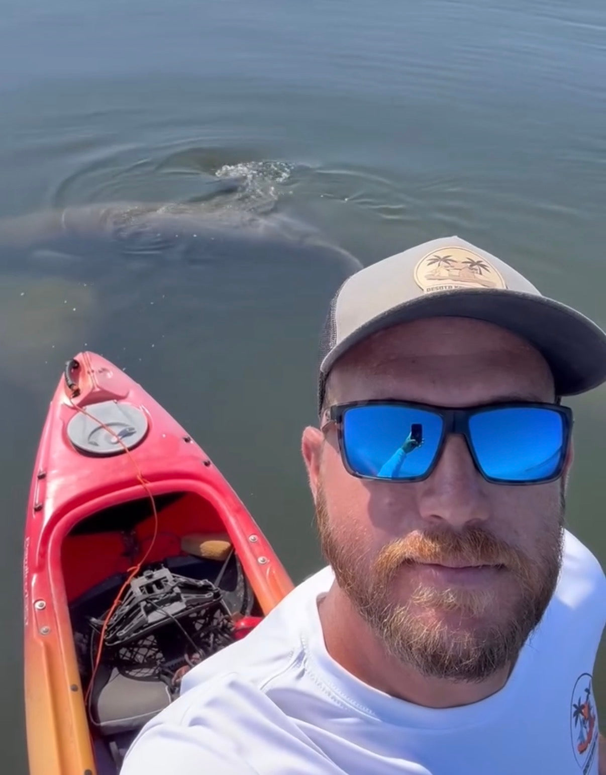 Man in a kayak with a manatee in the water behind him