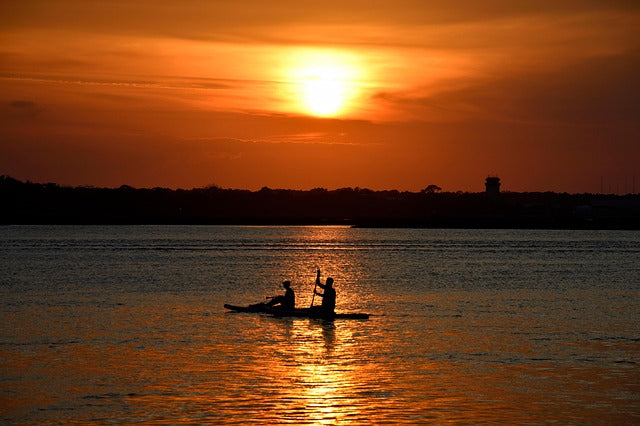 Two people on a tandem kayak at sunset.
